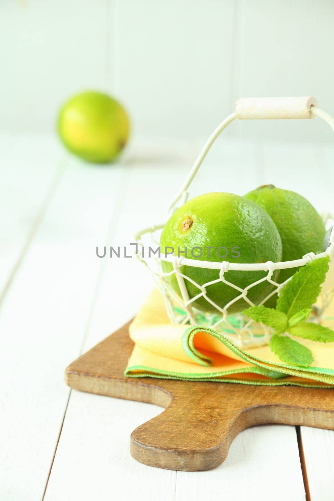 Fresh green limes in a wire basket on a yellow napkin and wooden board, bright high key image with copyspace
