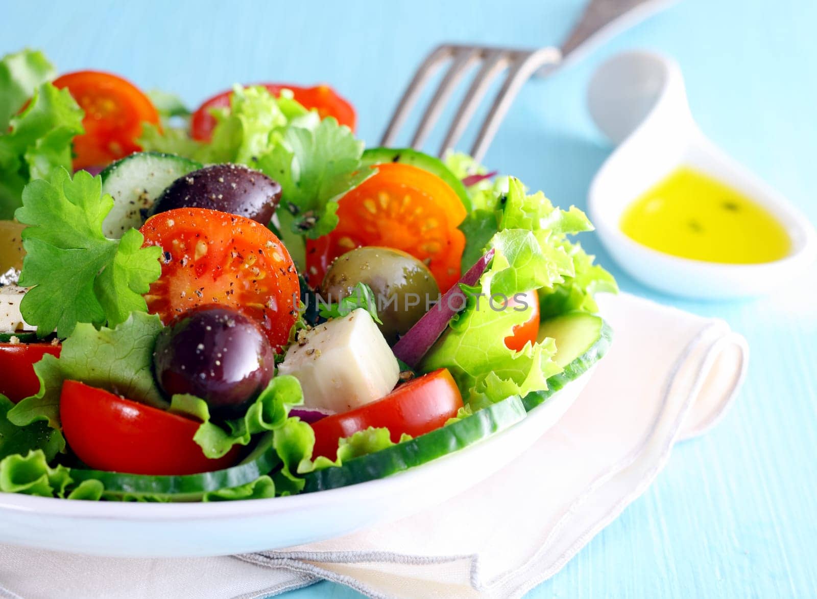 Healthy fresh Greek salad with olives and feta cheese nestling on a bed of crisp lettuce with tomato, closeup partial view of the dish