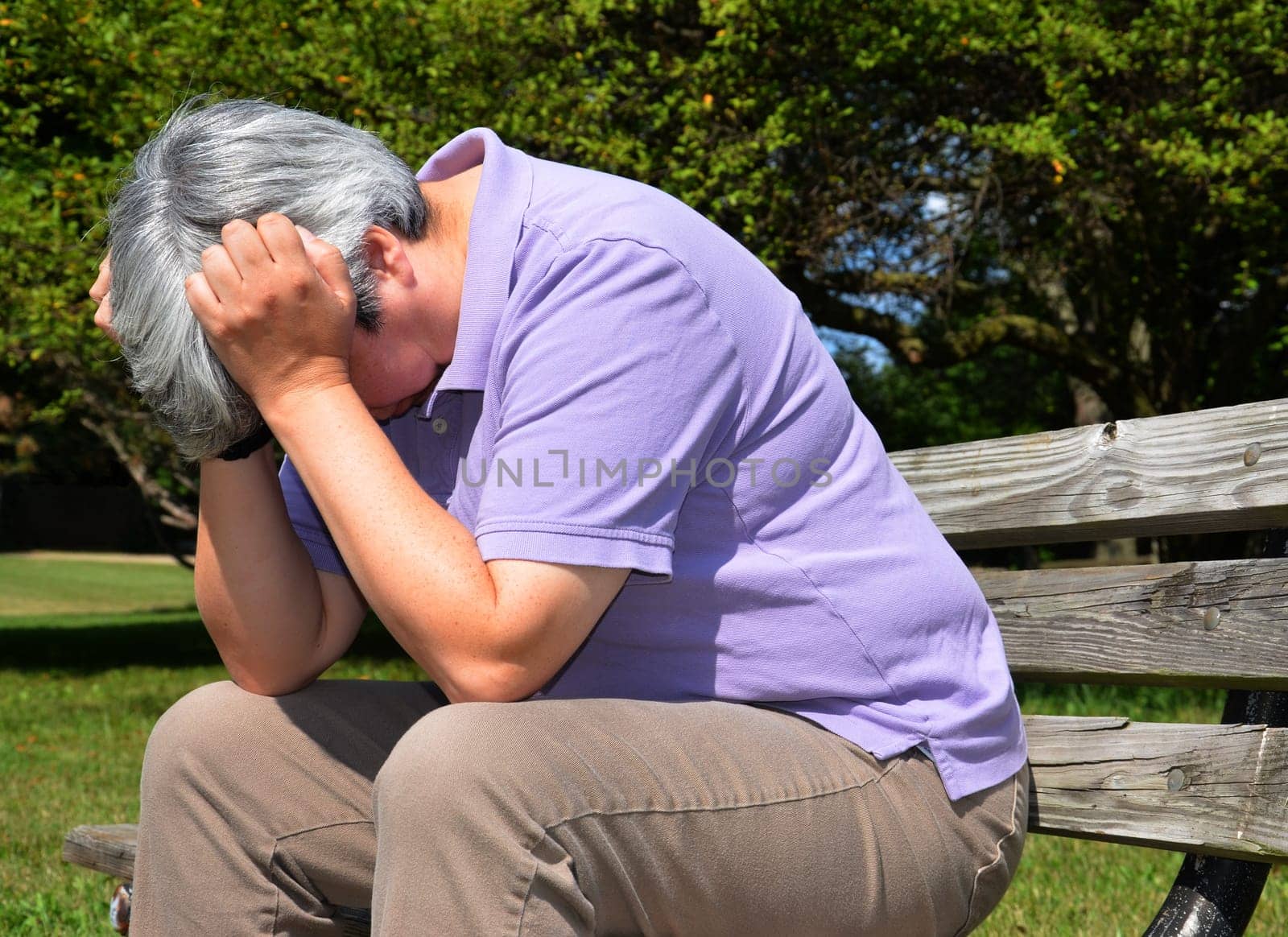 Older woman sitting on bench, head in hand in despair