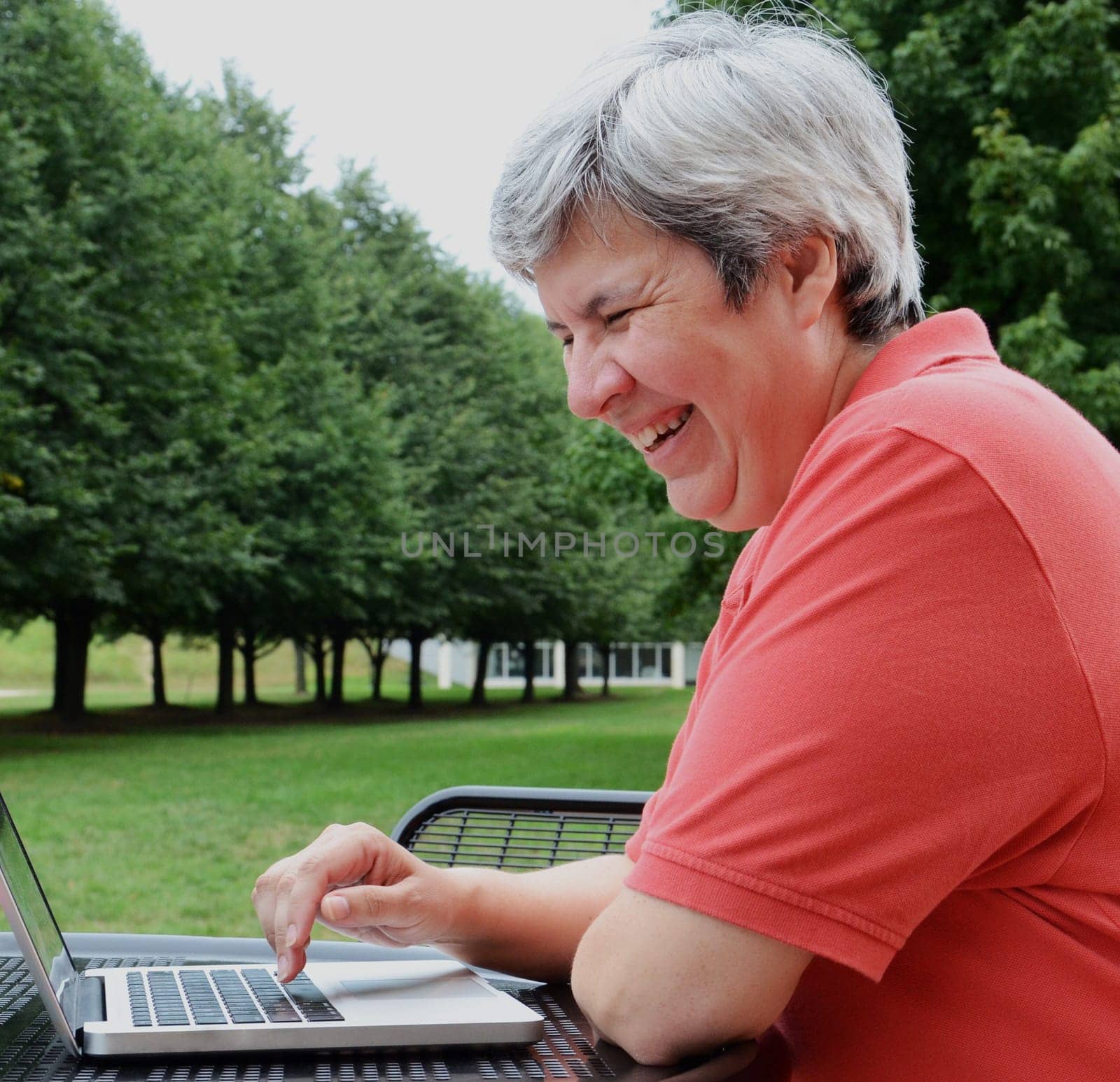 middle-aged woman browsing on laptop at table outside with trees