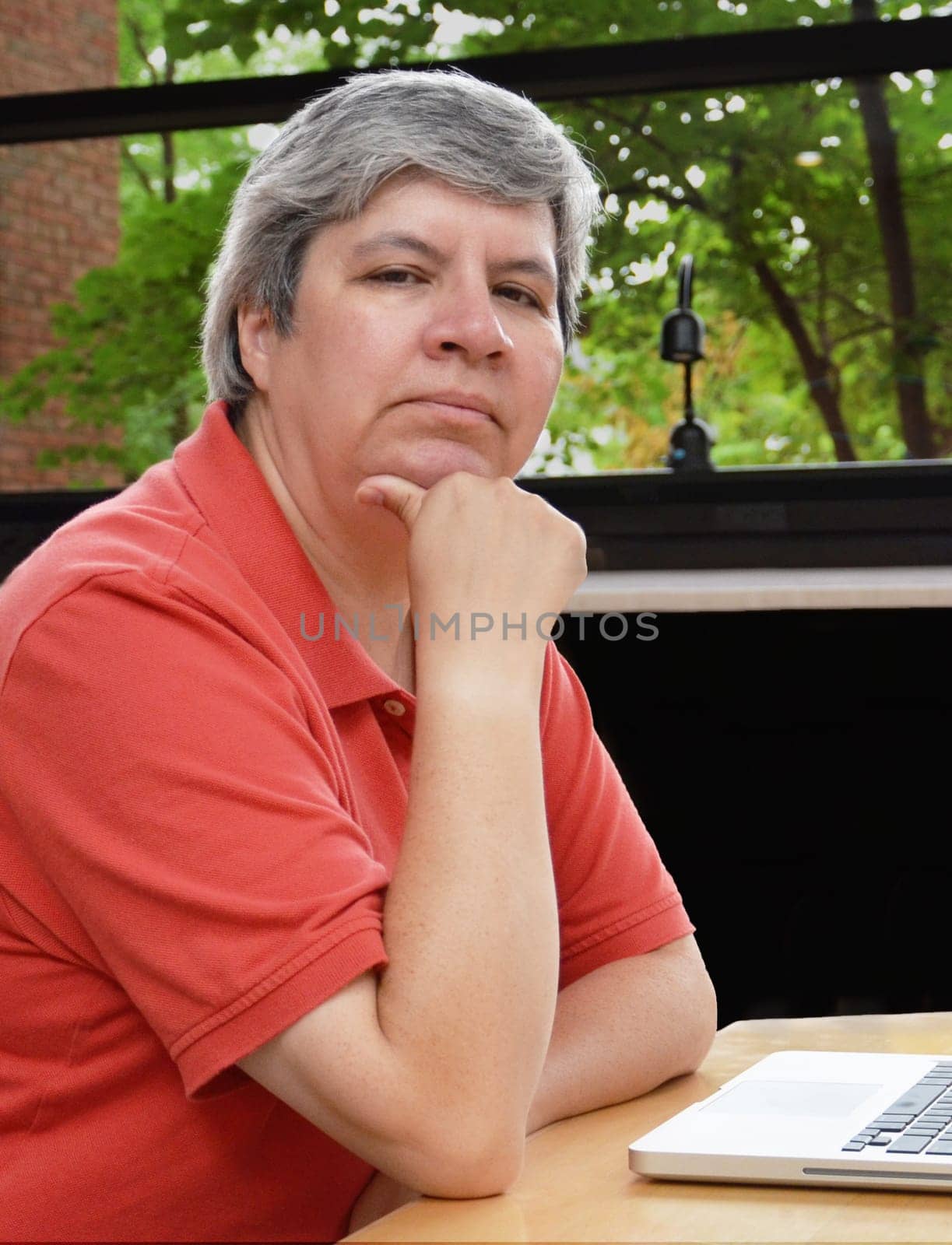 middle-aged woman seated at table with laptop, looking at you