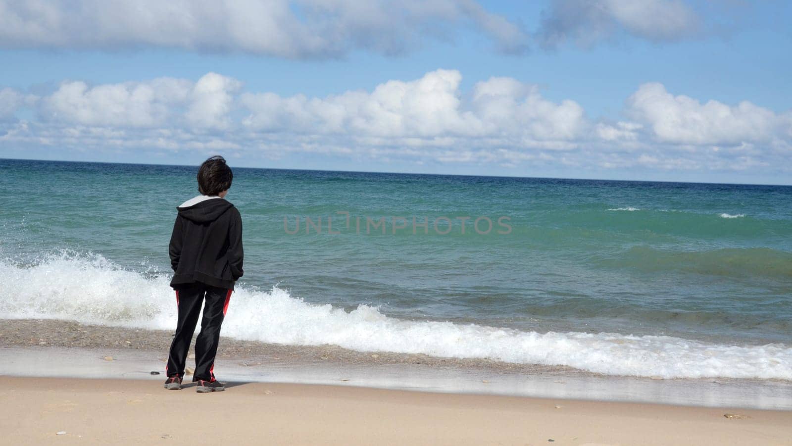 Boy watching waves wash ashore in Lake Michigan beach