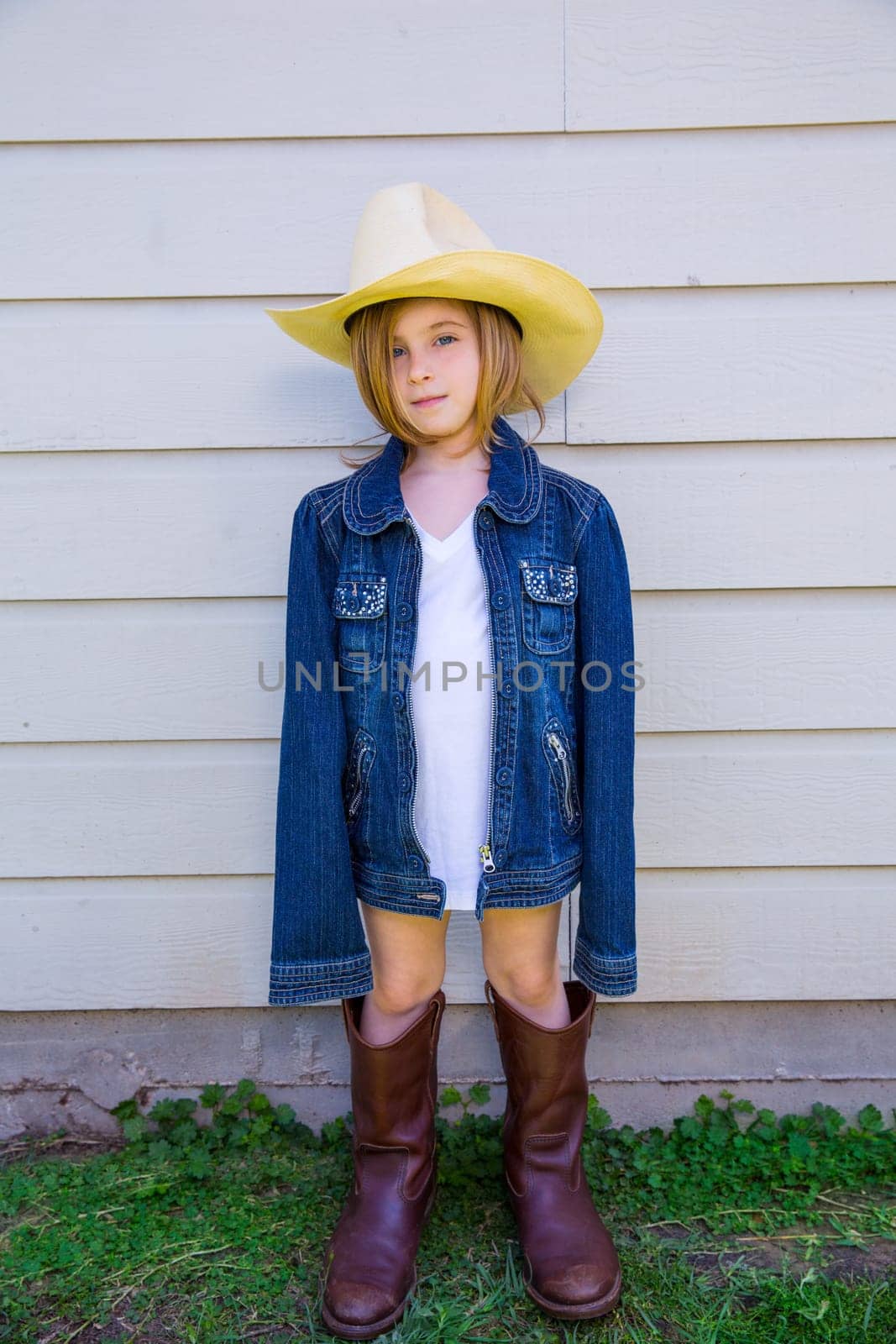Little kid girl pretending to be a cowboy with father boots and hat
