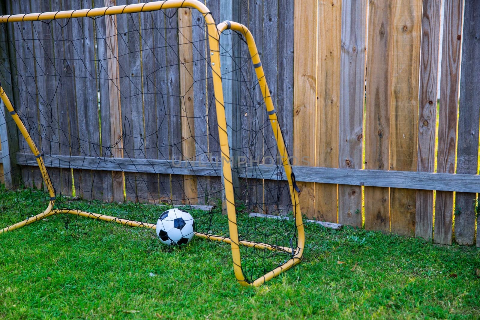 Backyard chldren soccer goal at the wood fence with leather ball on grass