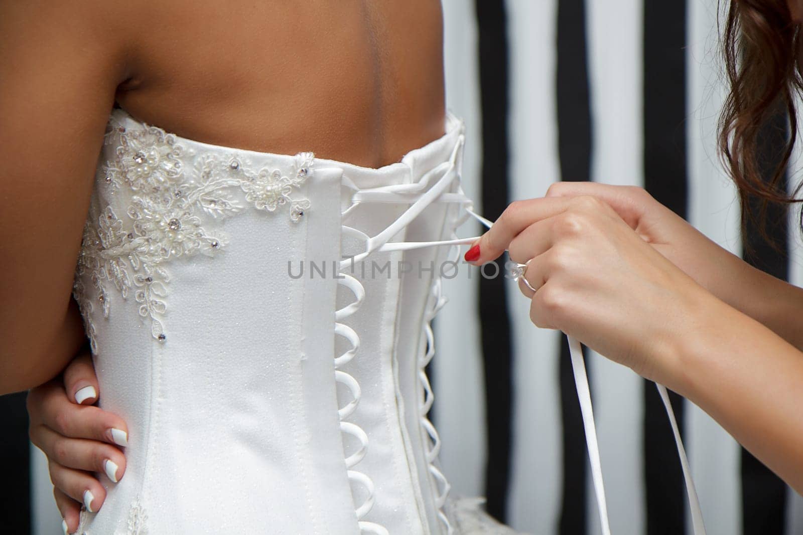 bridesmaid helps the bride to tie the corset