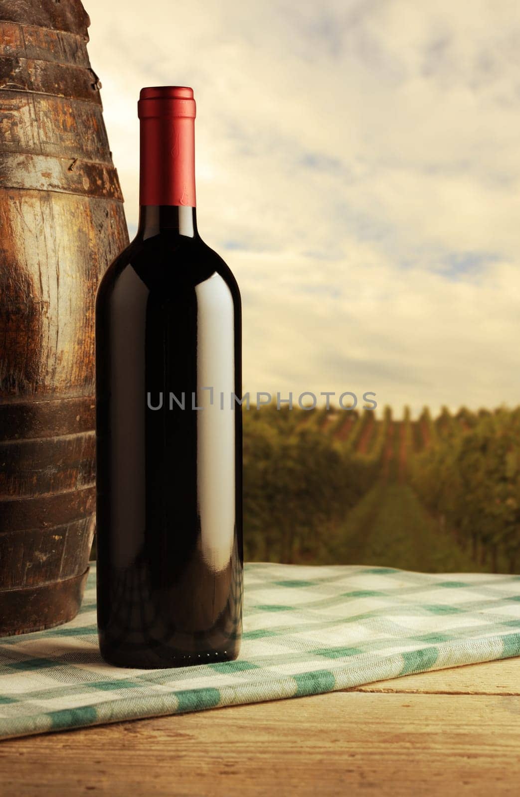 red wine bottle and wodden barrel, vineyard on background