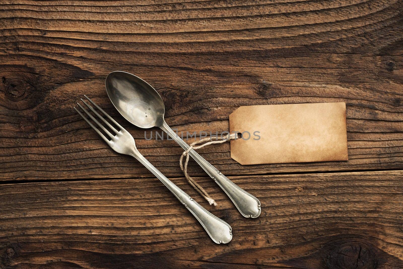 Old fork and spoon with paper label on wooden background