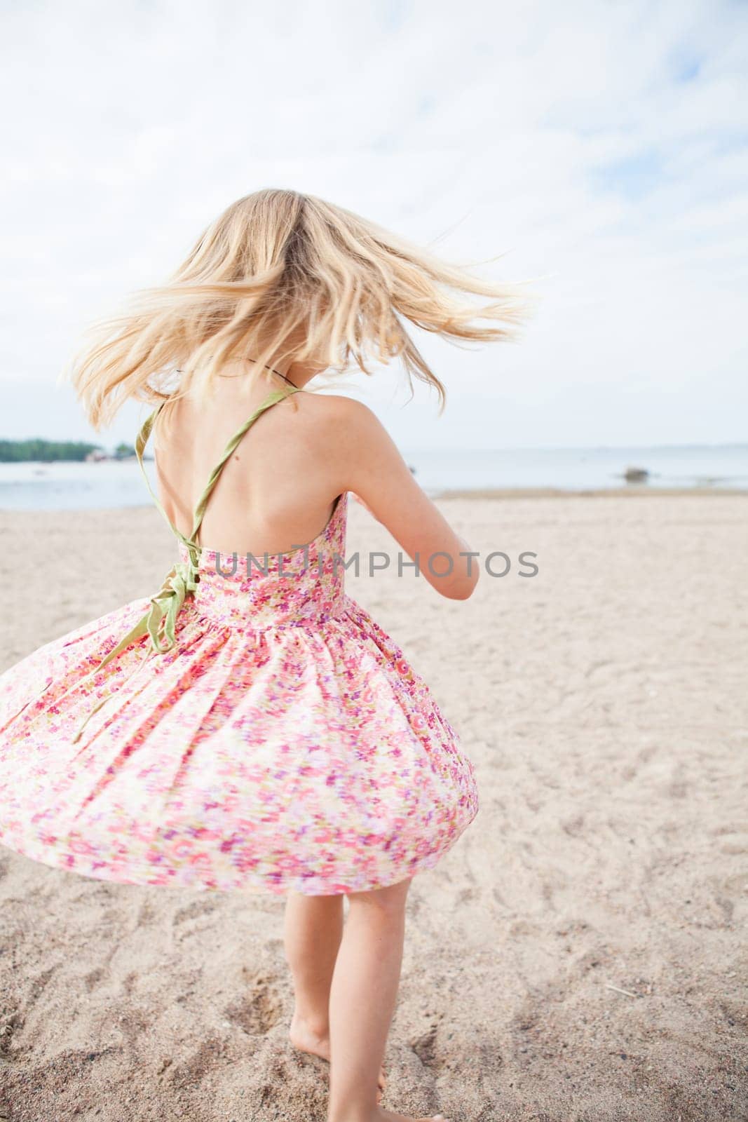 Young barefoot girl with pink patterned dress having fun at beach with ocean in background