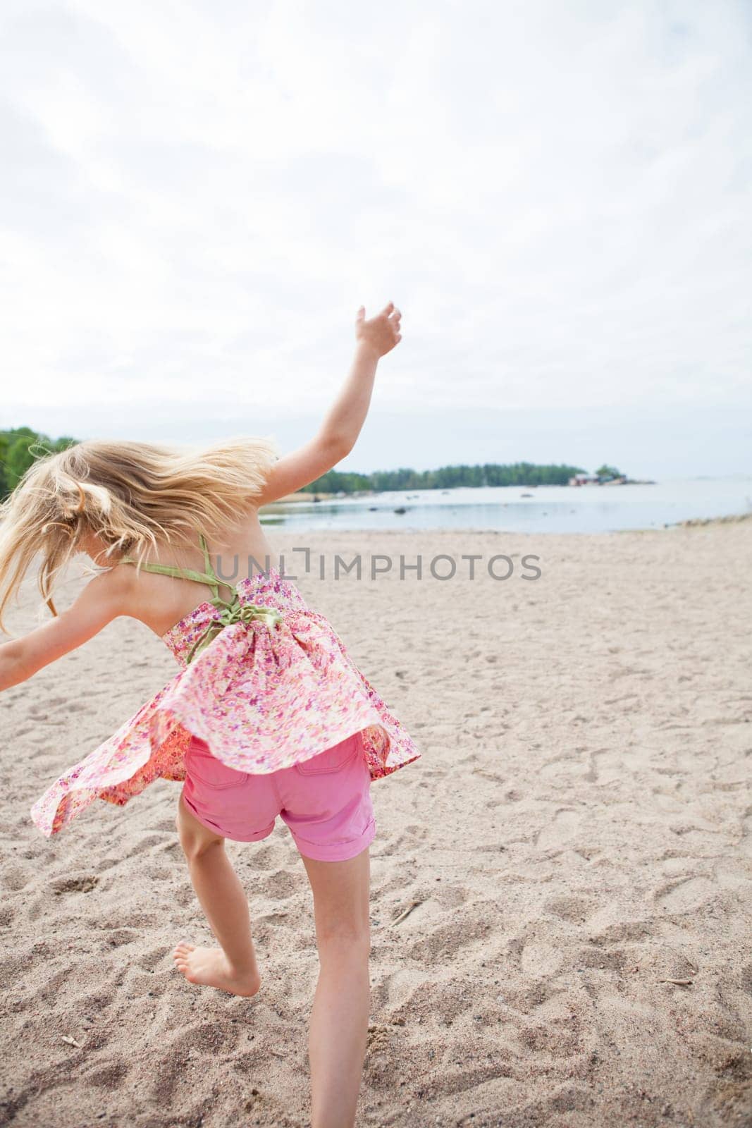 Young barefoot girl with pink patterned dress and pants having fun at beach with ocean in background