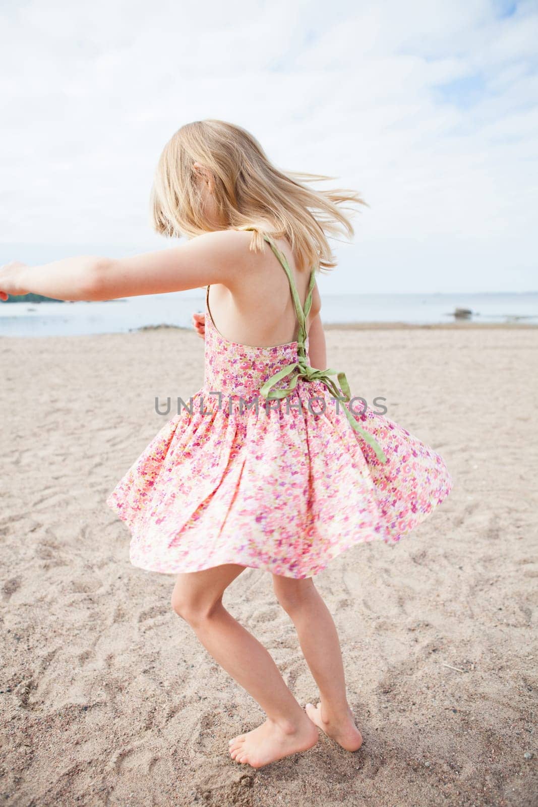 Young barefoot girl with pink patterned dress having fun at beach with ocean in background