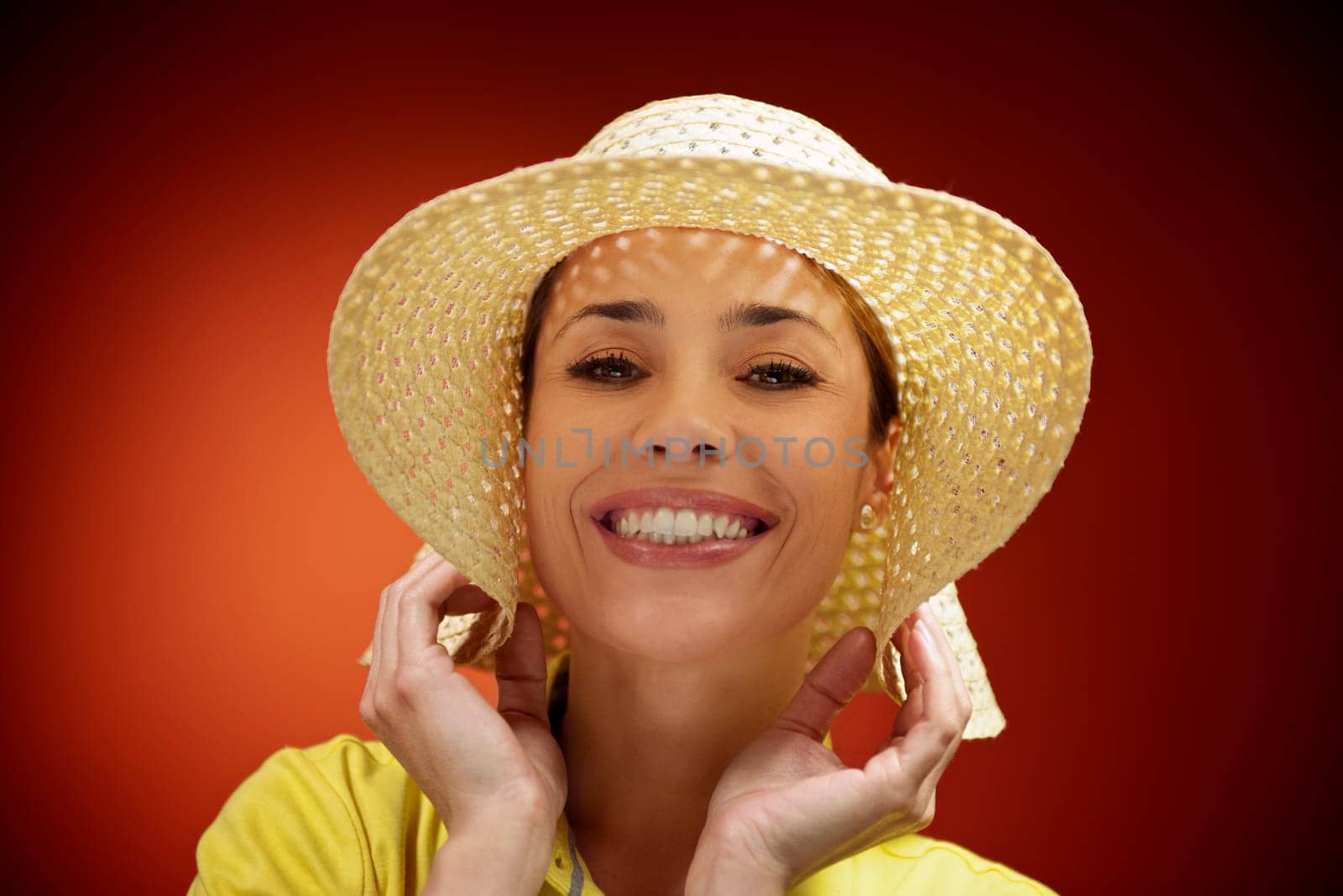 mid adult woman with straw hat smiling and looking at camera on red background