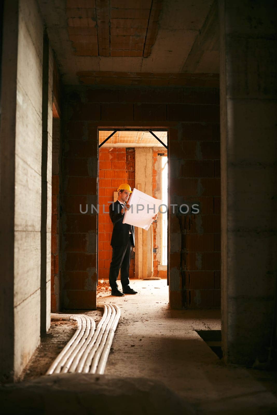 Engineer at work in construction site, standing in apartment building and looking at blueprints and plans