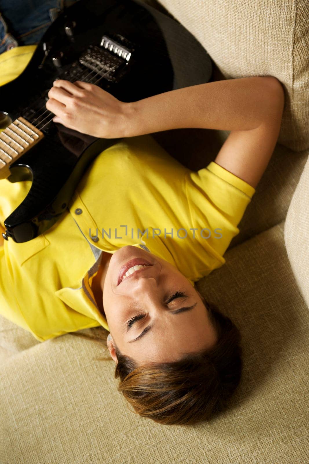 beautiful mid adult woman playing electric guitar at home, laying on sofa