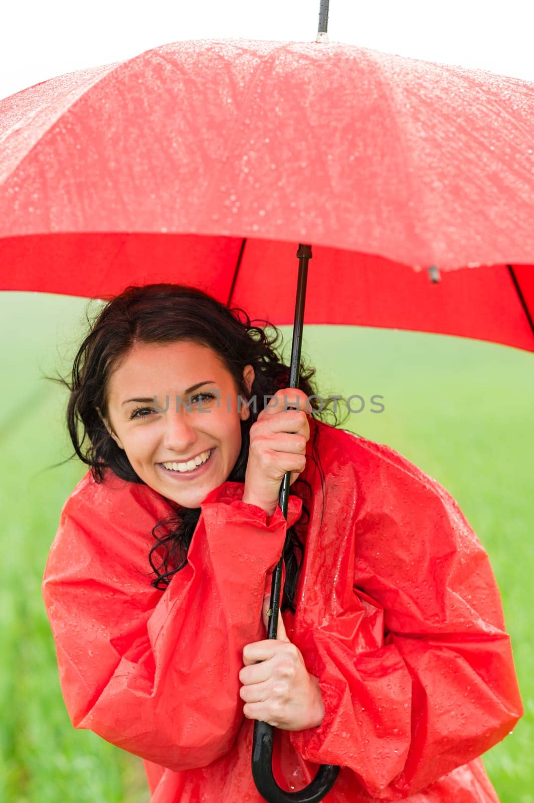 Wet young girl in raincoat enjoying rainfall with umbrella