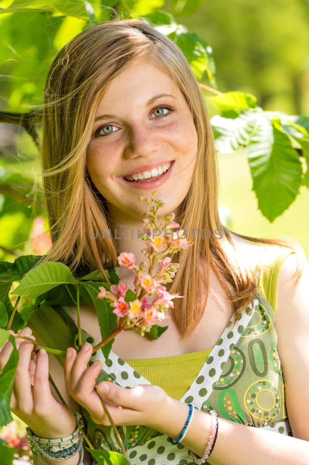 Smiling teenage girl smelling blooming tree in springtime