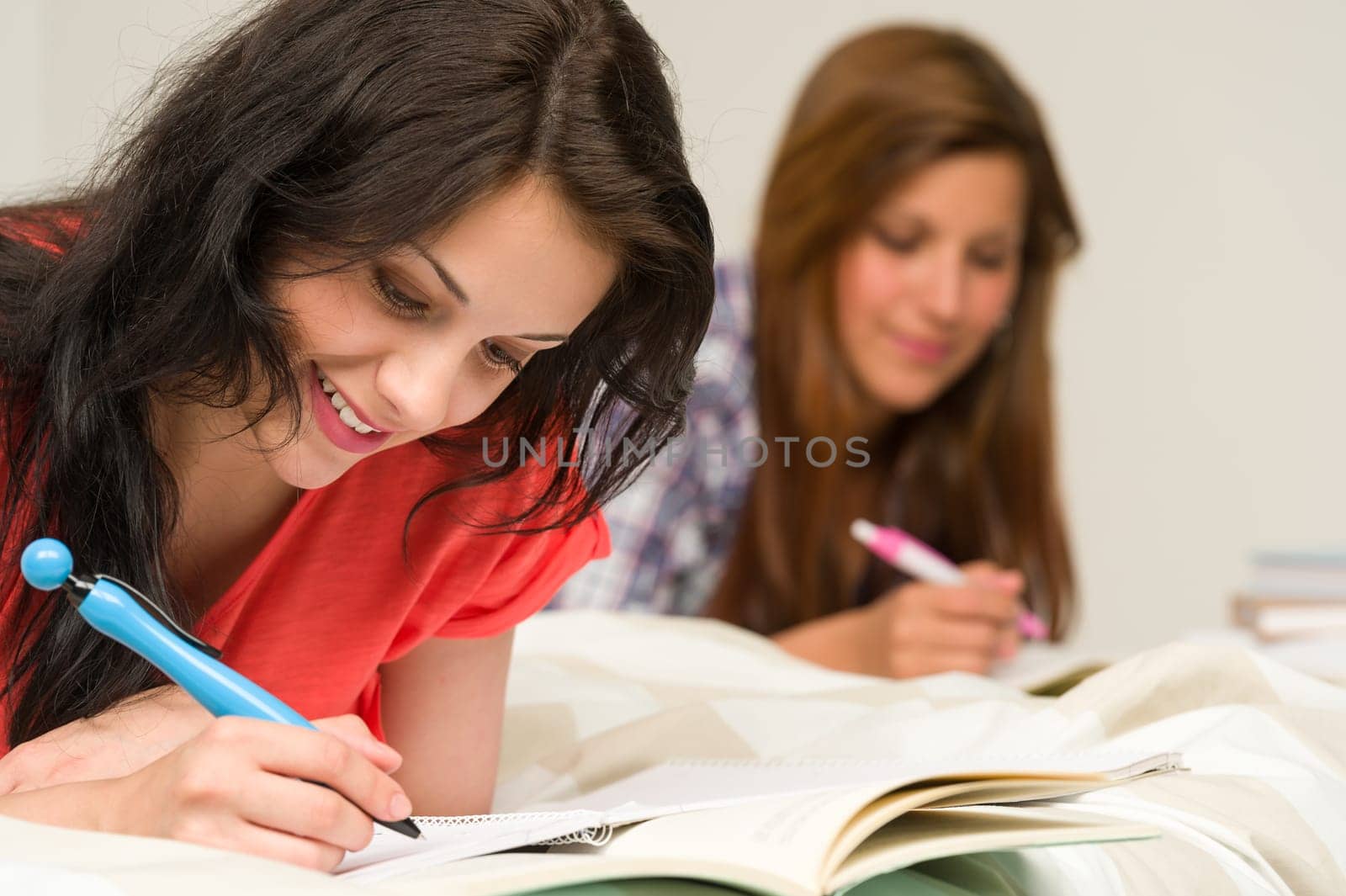 Young teenage girls lying and studying on bed