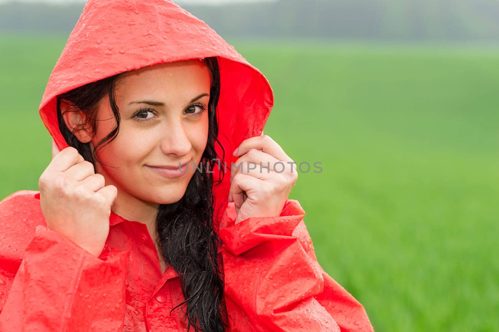 Adolescent girl smiling in the rain in red raincoat