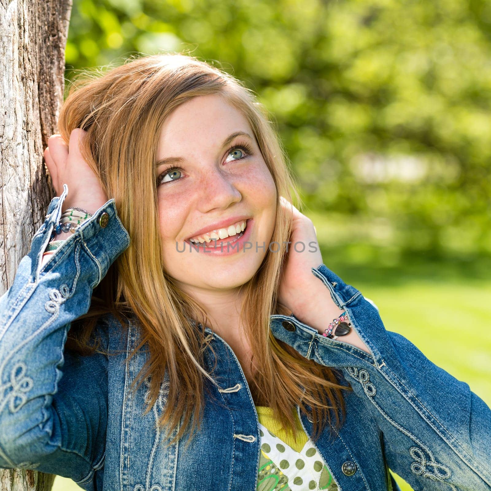Lively smiling girl enjoying nature and sunshine leaning against tree
