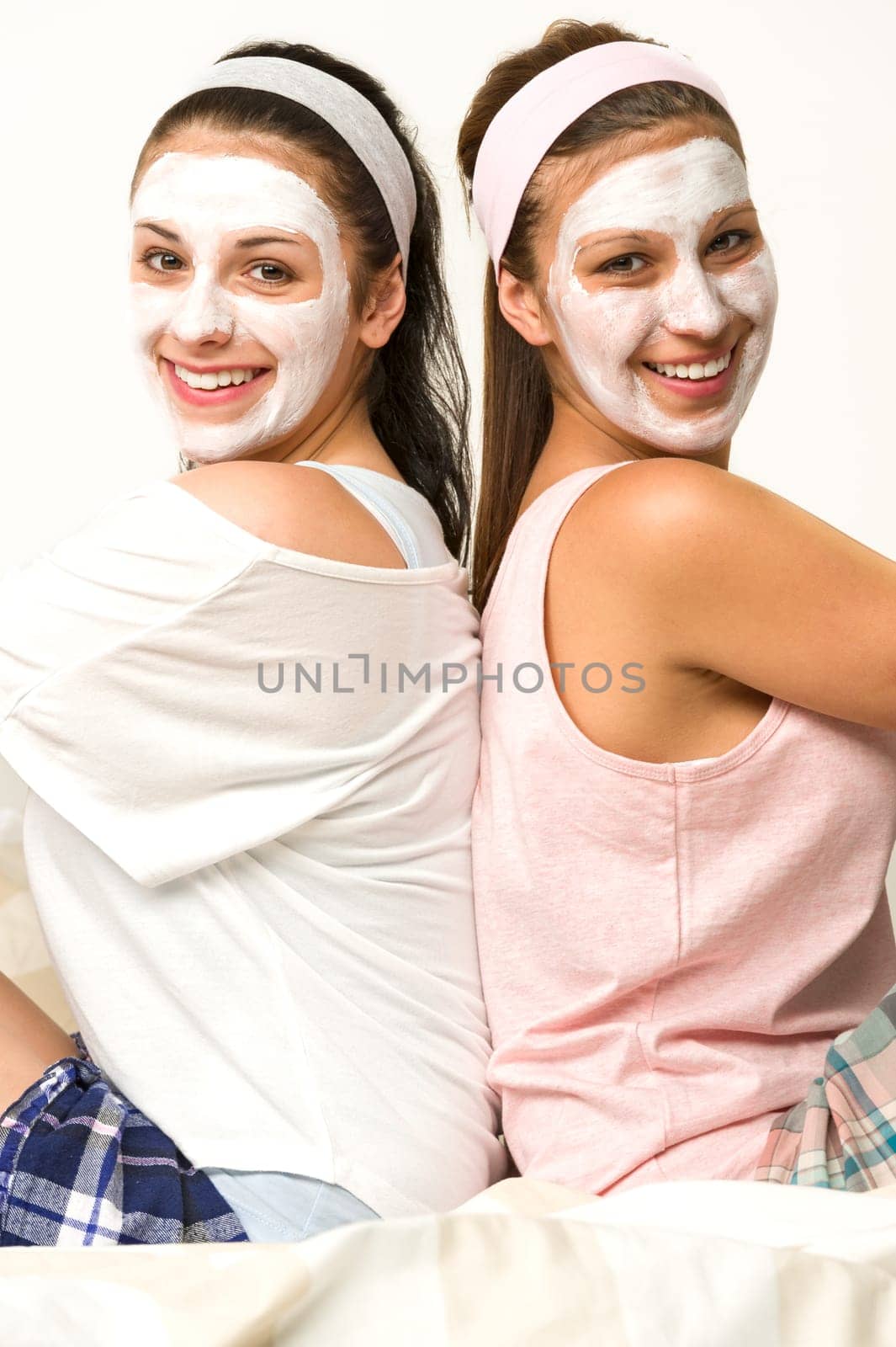 Two female friends sitting back-to-back with white facial mask