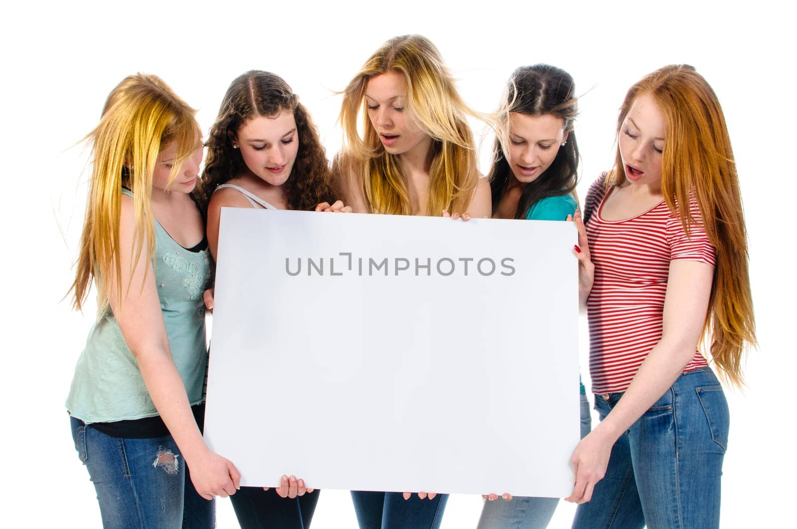 Five cute teenage girls holding a billboard add and looking at it, isolated over a white background.