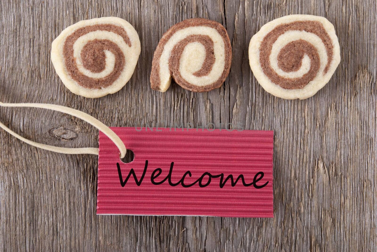 a red label with welcome on it and some cookies on a wooden background
