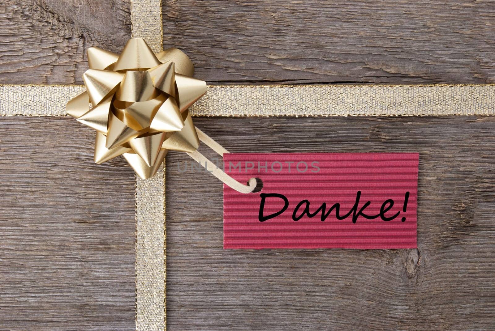 the german word Danke which means thanks on a red label on a gift bow with wooden background