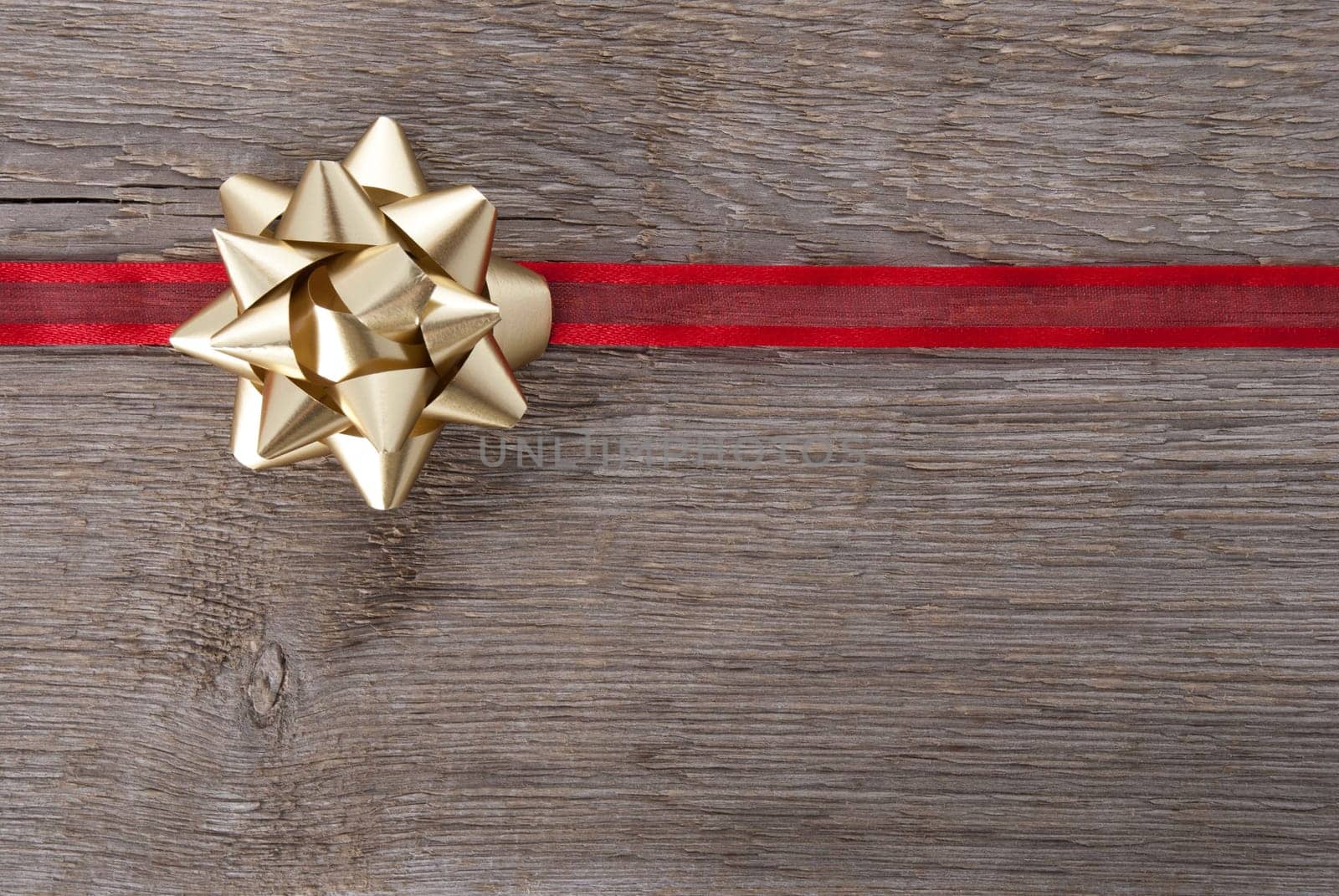 a golden bow on a red ribbon on wood as background with copy space