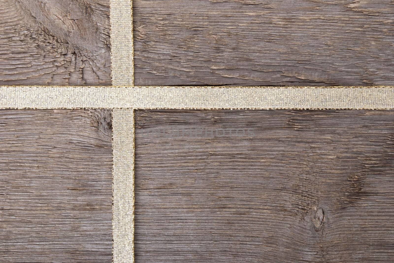 golden ribbon in form of a cross on wood as gift background