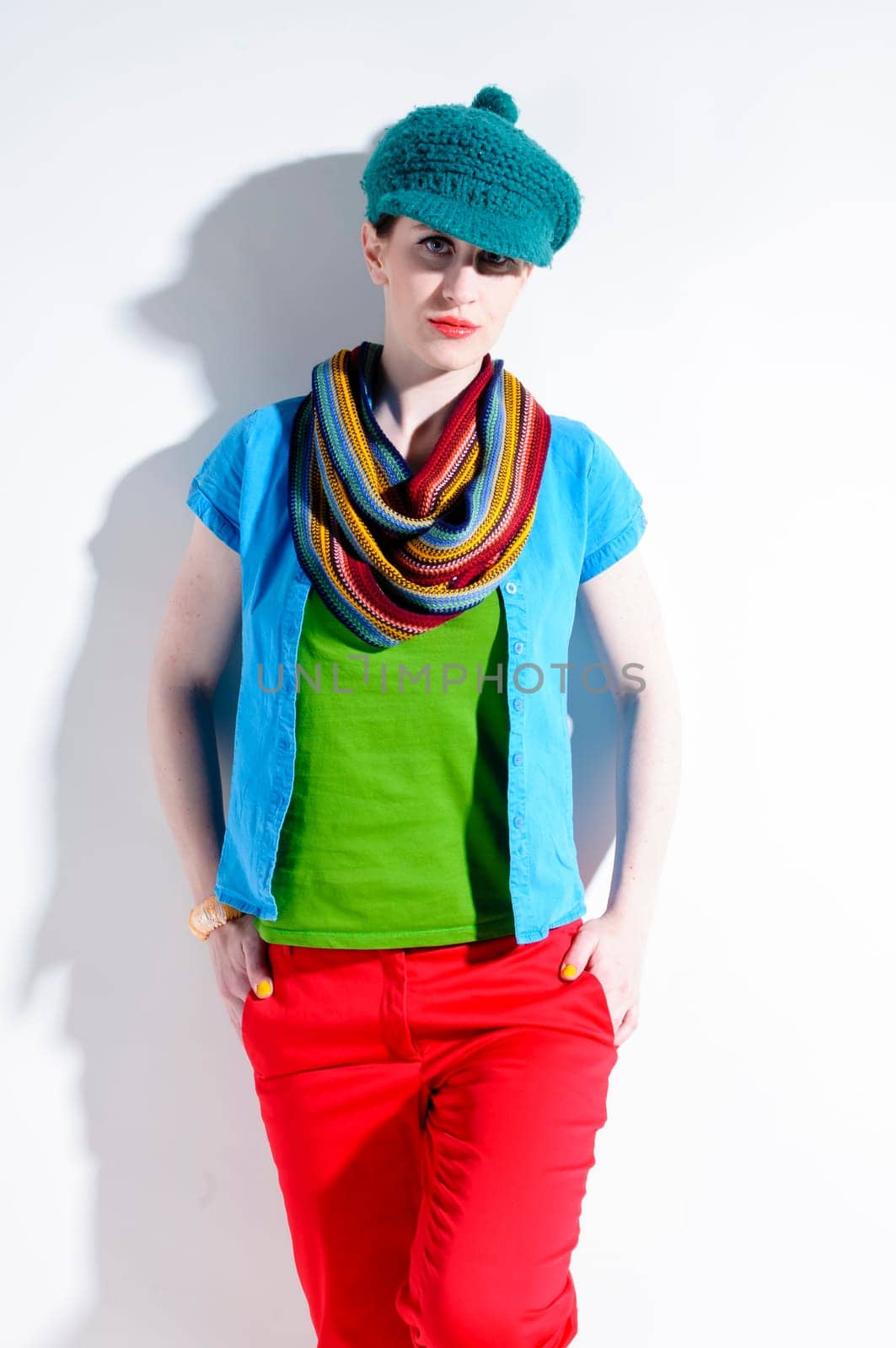 Young woman with black straight hair wears colorful mixed clothes and stands in front of a white background.