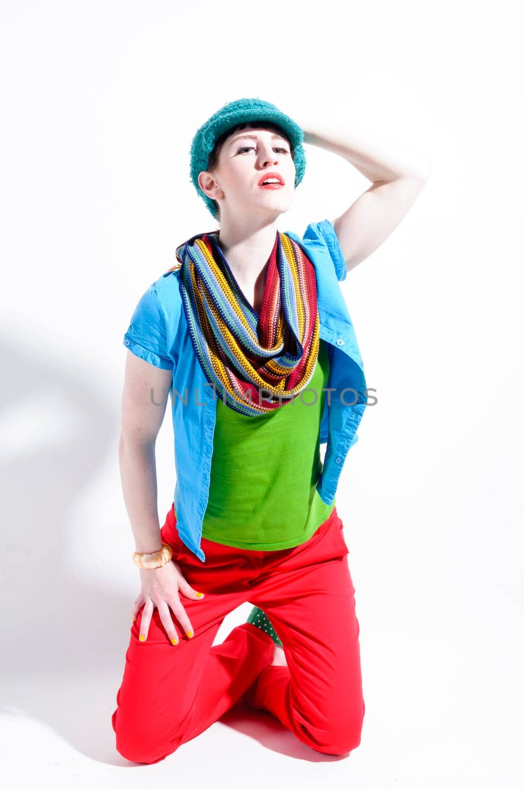 Young woman with black straight hair wears colorful mixed clothes and stands in front of a white background.