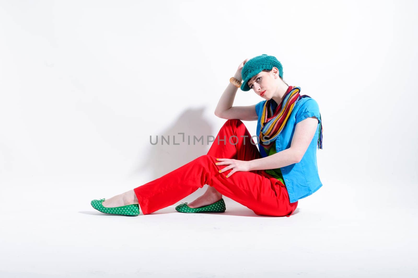 Young woman with black straight hair wears colorful mixed clothes and stands in front of a white background.