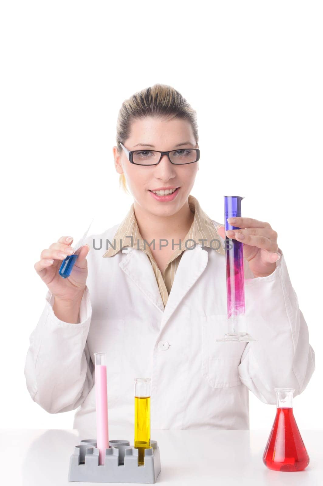 Attractive young chemist with blond hair and glasses wears a white coat and pours various colored chemicals together in test tubes,exposed against a white background