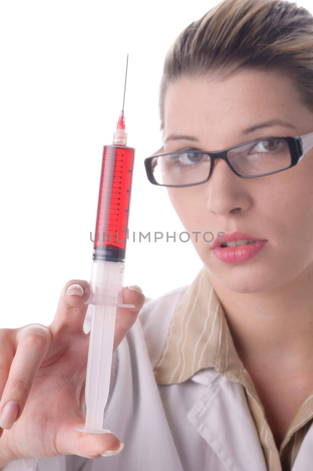 Attractive young doctor with blond hair wears a white coat and holds a large syringe with a red liquid in front of the camera,exposed against a white background.