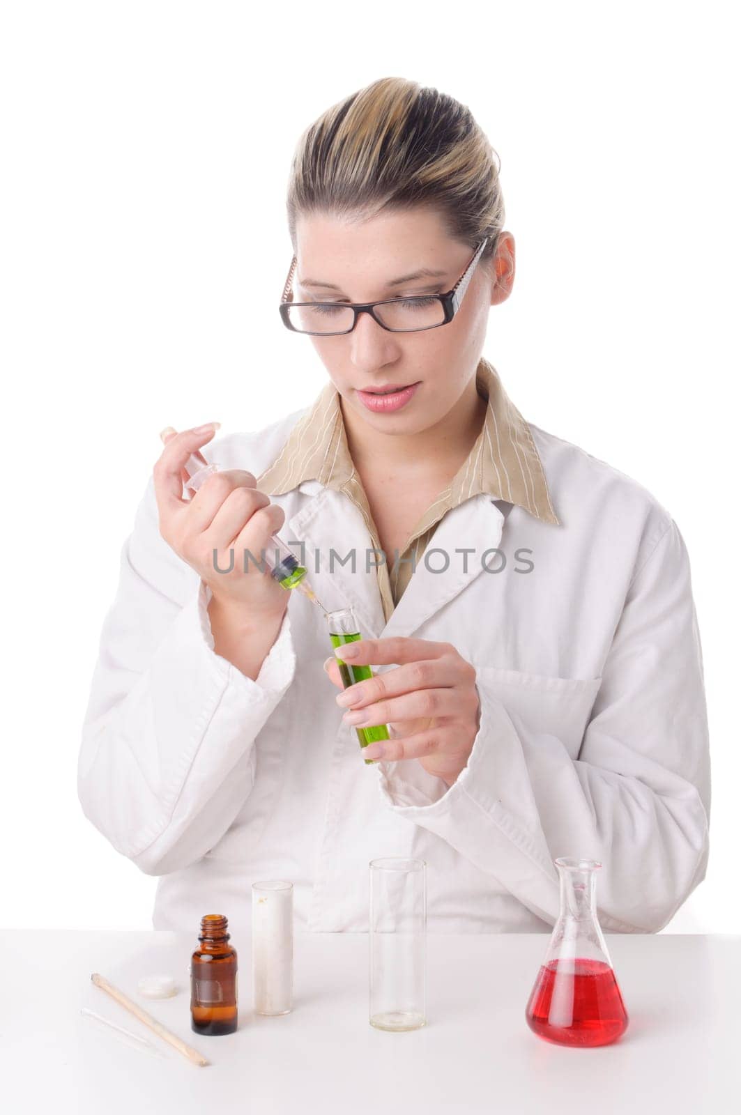 Attractive young chemical laboratory assistant with blond hair and glasses works with various colored liquids in test tubes,exposed against a white background. On the table are various colored chemicals.