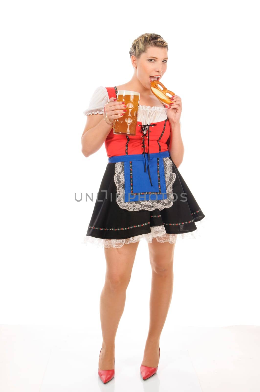 Young attractive woman with blond hair and braids wears a colorful dirdl dress and holds a pretzel and a beer mug with freshly tapped beer in her hand,exposed against a white background.
