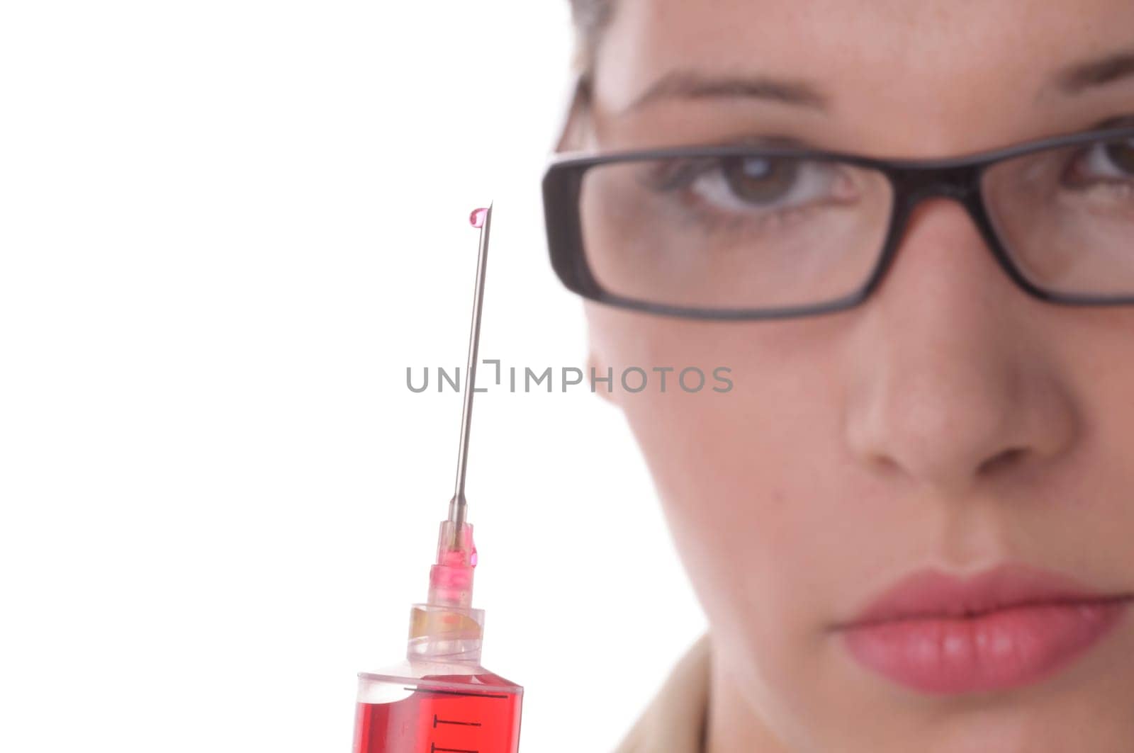 Attractive young doctor with blond hair wears a white coat and holds a large syringe with a red liquid in front of the camera,exposed against a white background.