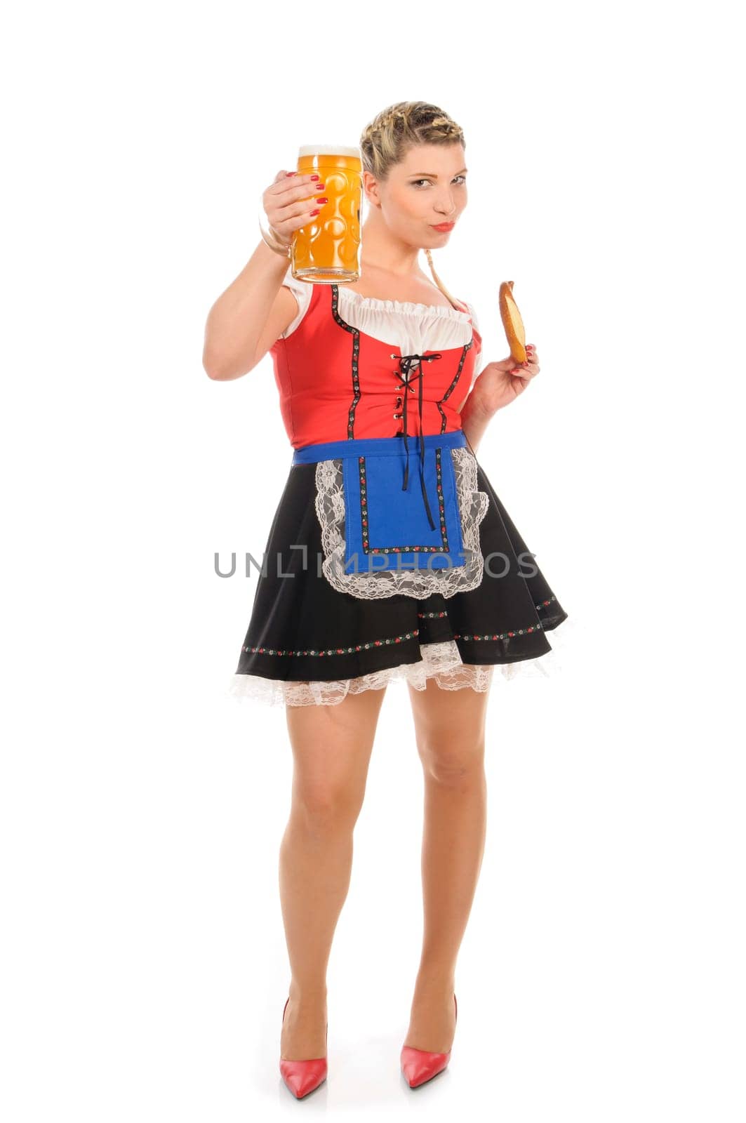 Young attractive woman with blond hair and braids wears a colorful dirdl dress and holds a pretzel and a beer mug with freshly tapped beer in her hand,exposed against a white background.