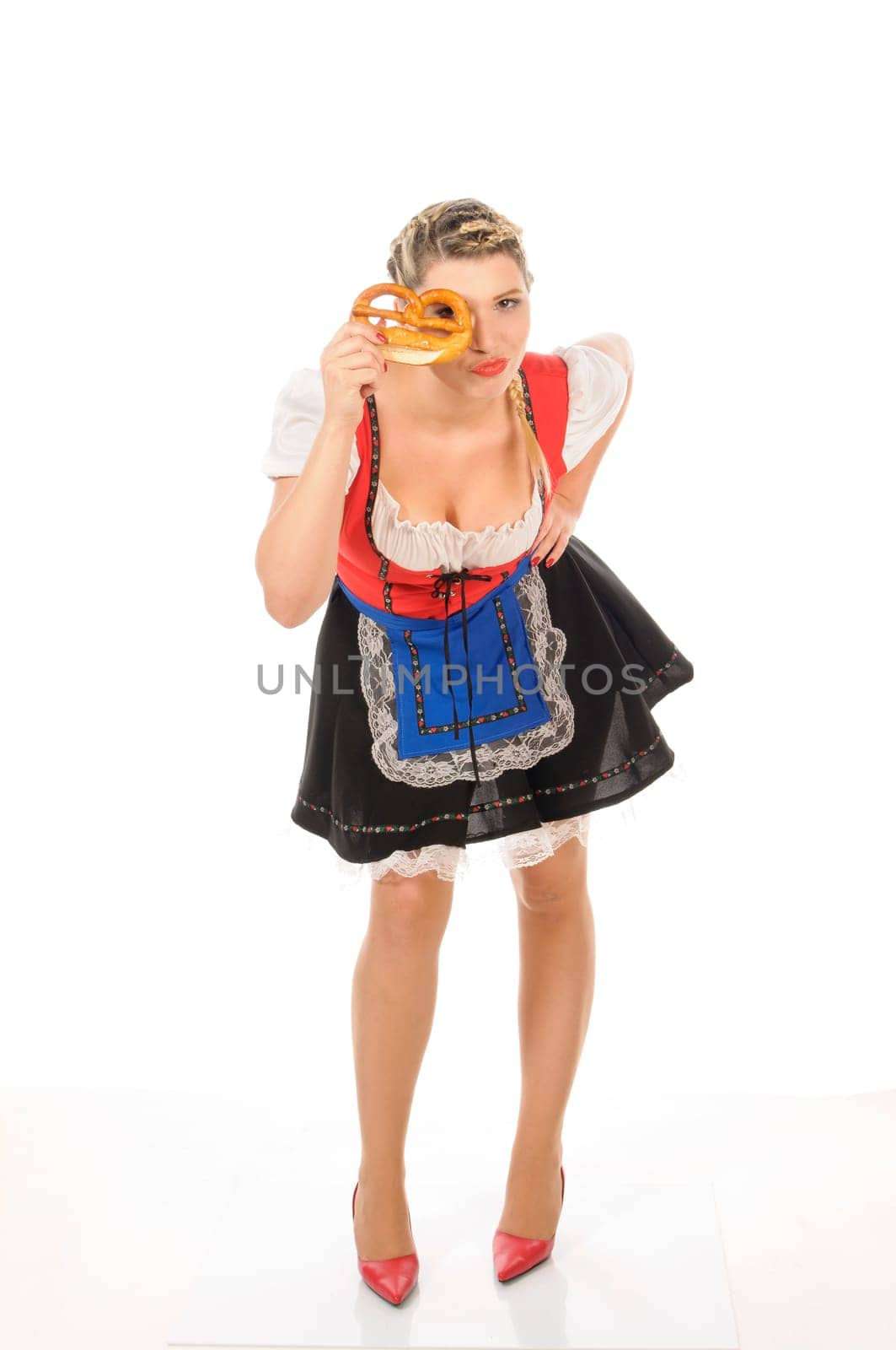 Young attractive woman with blond hair and braids wears a colorful dirdl dress and holds a pretzel in her hand,exposed against a white background.