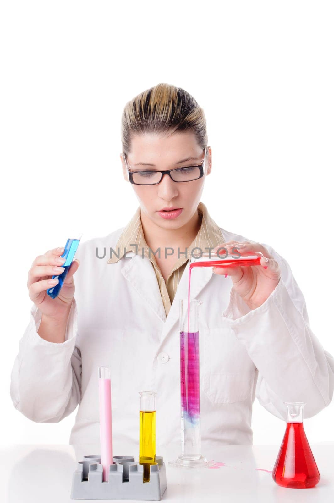 Attractive young chemist with blond hair and glasses wears a white coat and pours various colored chemicals together in test tubes,exposed against a white background