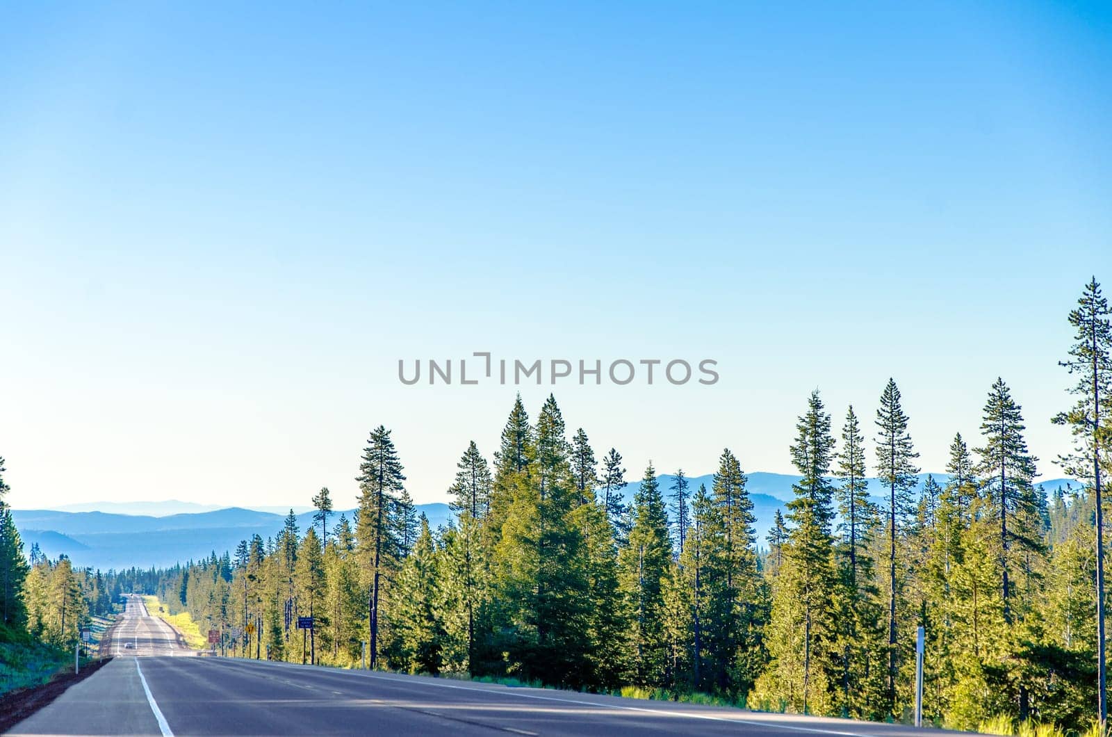 Long scenic highway passing through a lush green forest with blue hills in the background near Bend, Oregon