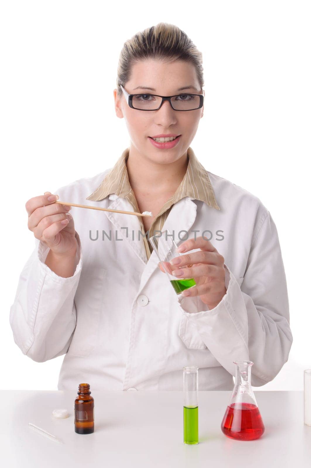 Attractive young chemical laboratory assistant with blond hair and glasses works with various colored liquids in test tubes,exposed against a white background. On the table are various colored chemicals.