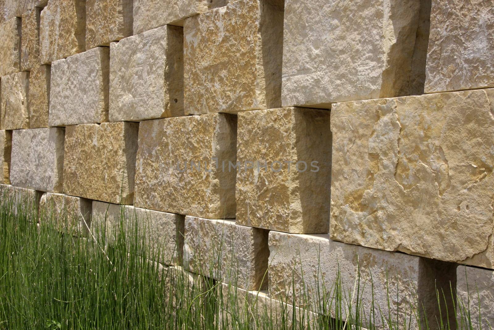 Background of a beige natural stone wall with green grass in front
