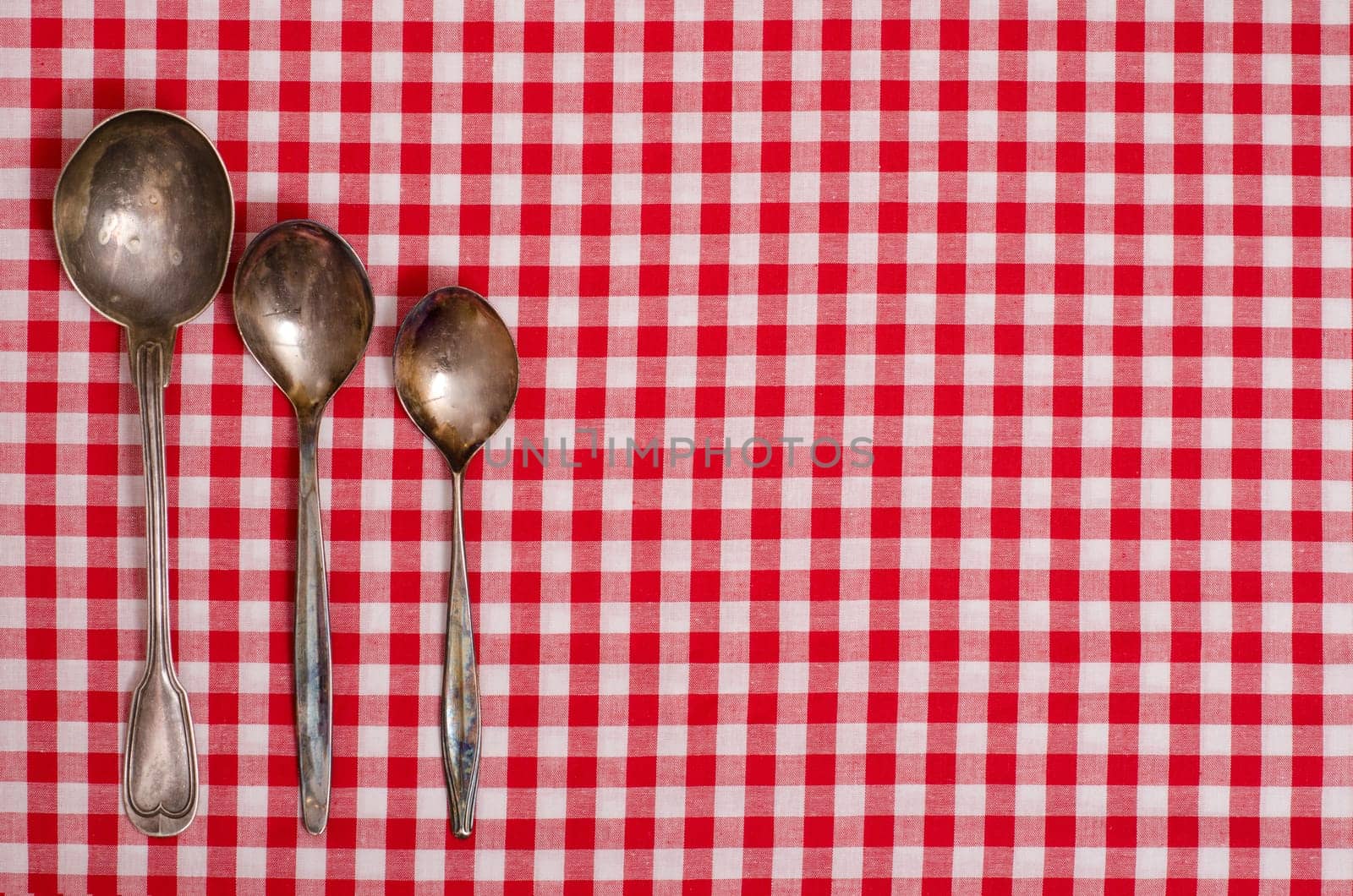 Three silver spoons on a table with red checkered cloth