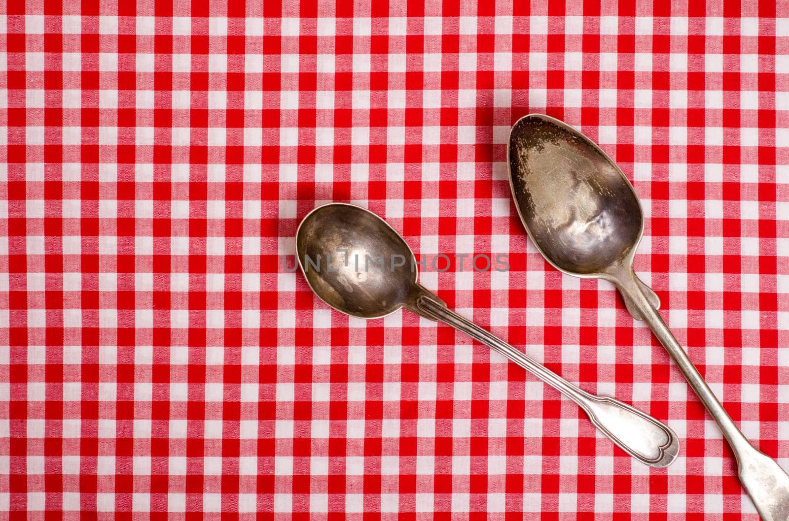 Two old silver spoons on a red and white checkered tablecloth