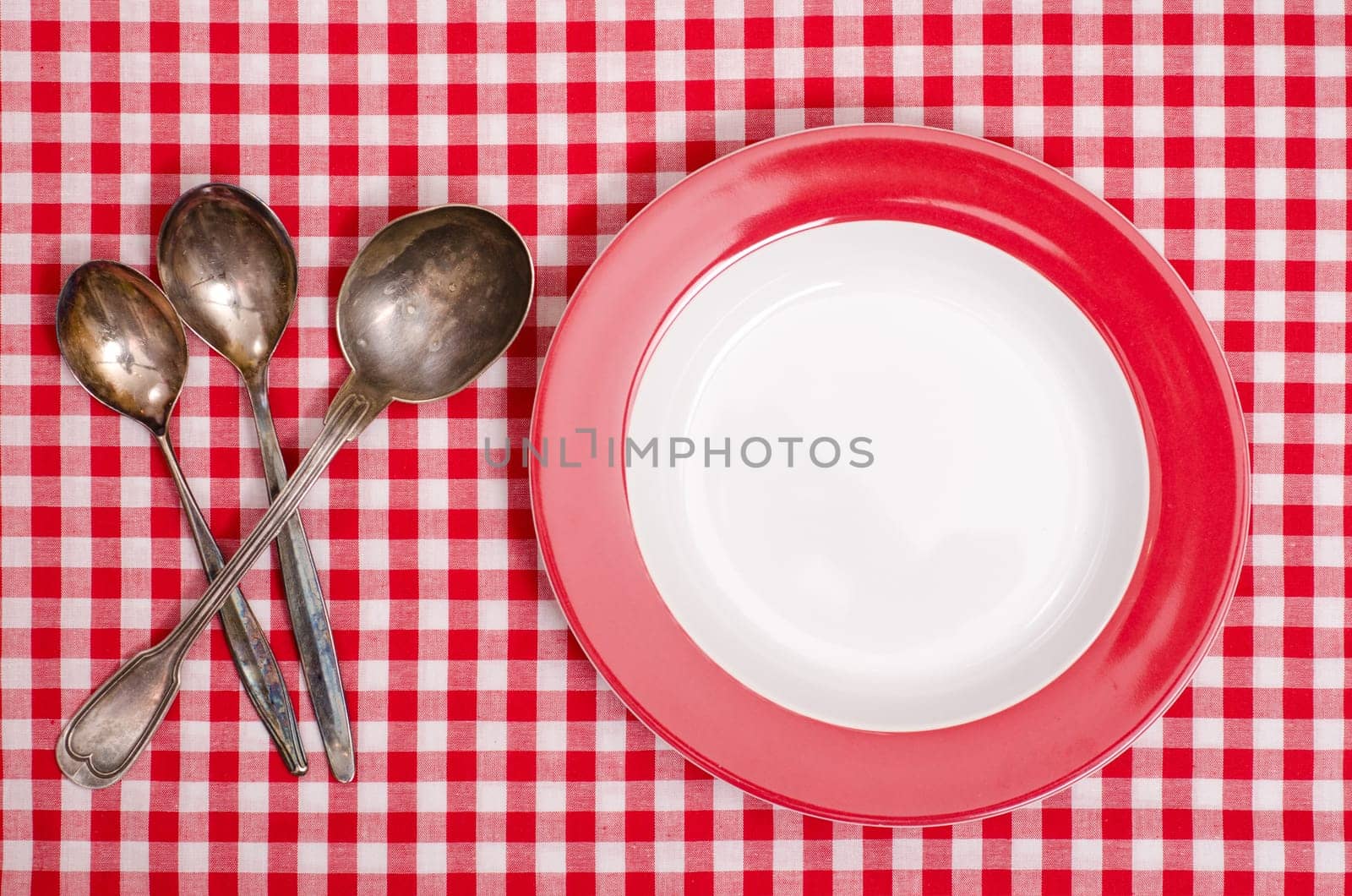 Three spoons made of silver and red plate on checkered cloth