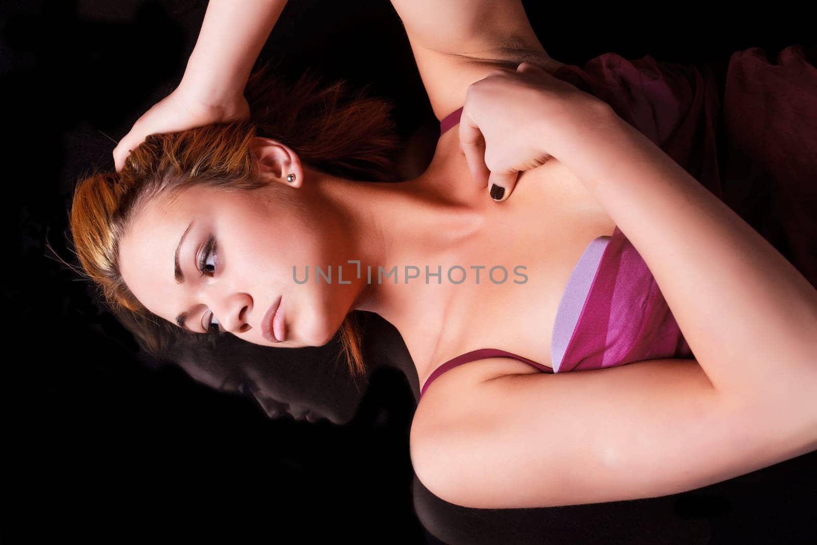 Sensual blonde girl in underwear lie and reflecting on dark background