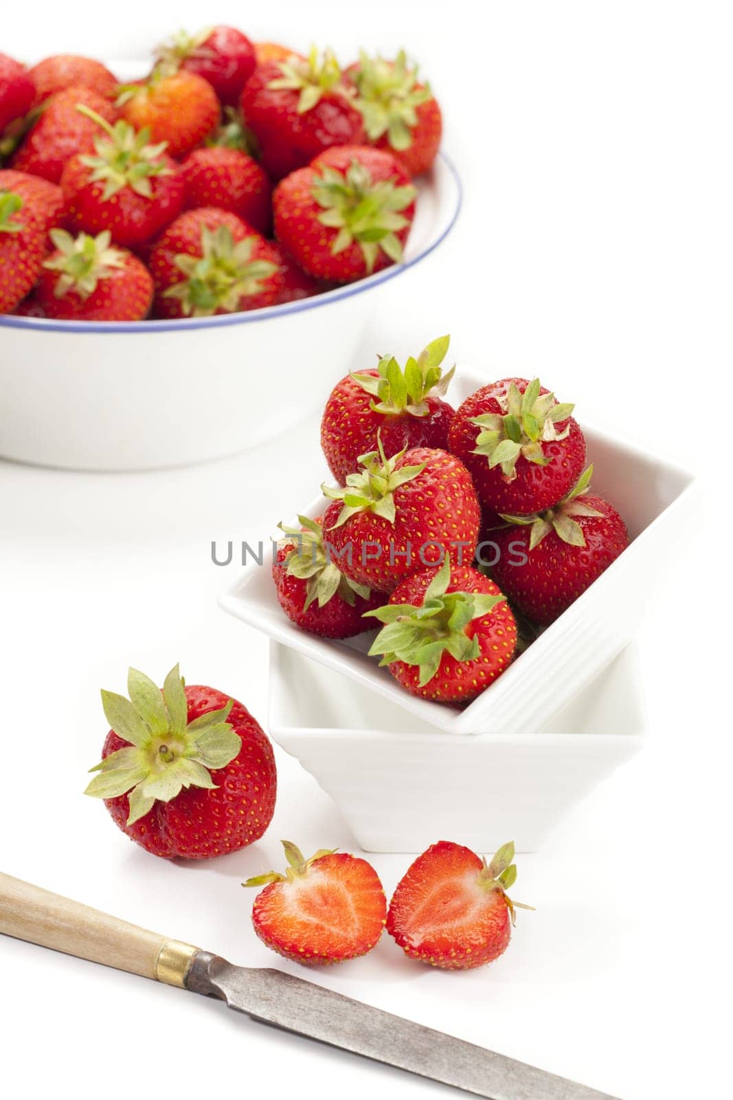 New strawberries in a white porcelain bowl and an enamel bowl with a knife in front of it,insulated against a white background