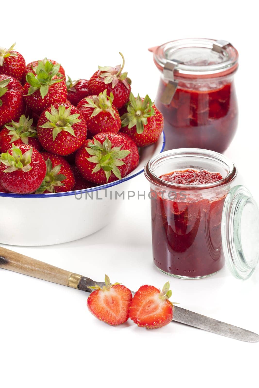 New strawberries in a white enamel bowl and homemade jam in jars against a white background