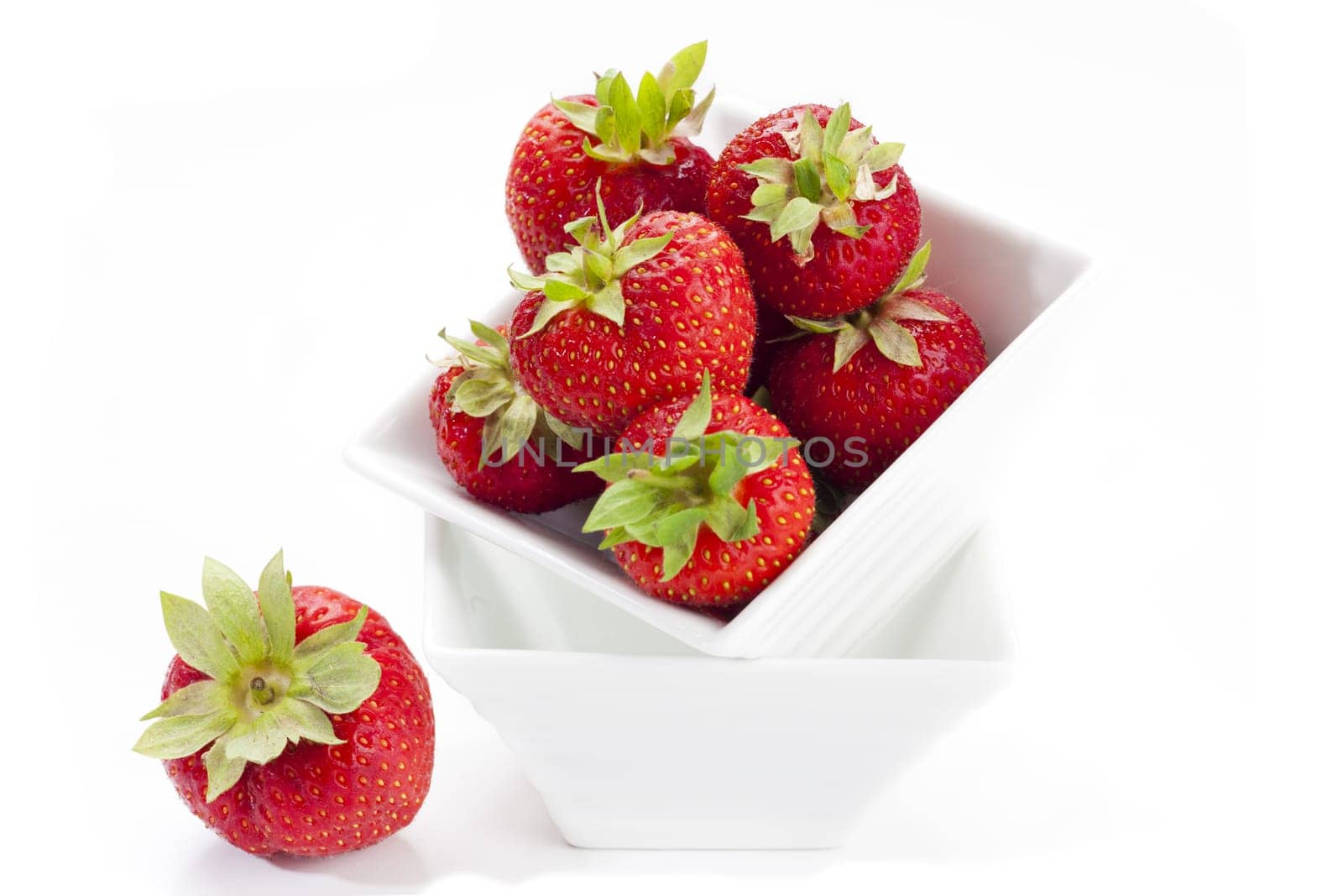Freshly harvested red strawberry in a white porcelain bowl against a white background