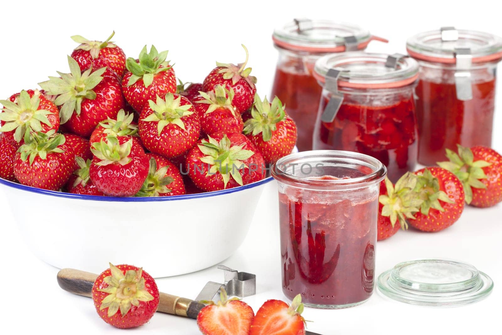 Homemade strawberry jam in jars and fresh strawberries in a bowl against a white background